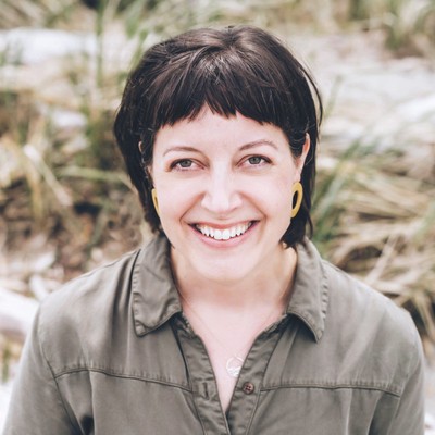 lisa-hemingway, a woman with short dark-brown hair who’s wearing a khaki blouse, smiles while standing outside in a grassy area