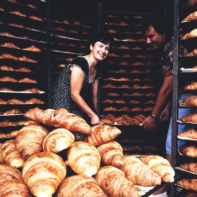 a woman and a man hold a tray while surrounded by racks and racks full of fresh-baked croissants (photo credit: harvard business review)