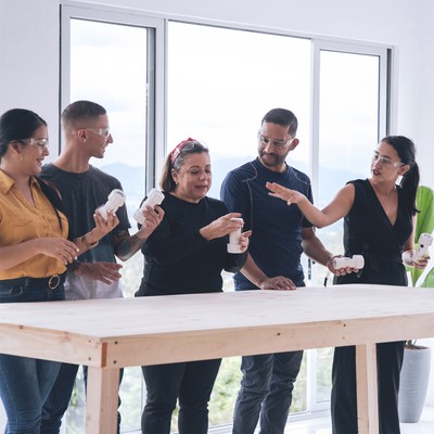 during an onsite workshop, ta leads four participants (two women and two men) in the reflection while standing near a wooden workbench