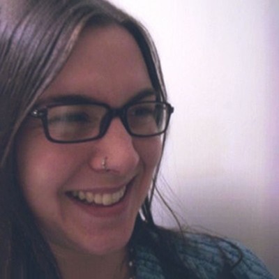 jennifer hogg, a woman with dark shoulder-length hair who’s wearing glasses and a nose ring, smiles