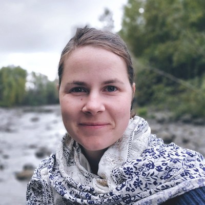 emily mcgill, a brunette woman who’s wearing a sweater, smiles while standing outside near a river