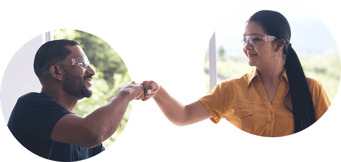 a fist bump between a man and a woman during one of smith assembly’s onsite workshops (both are wearing safety goggles and smiling at each other)