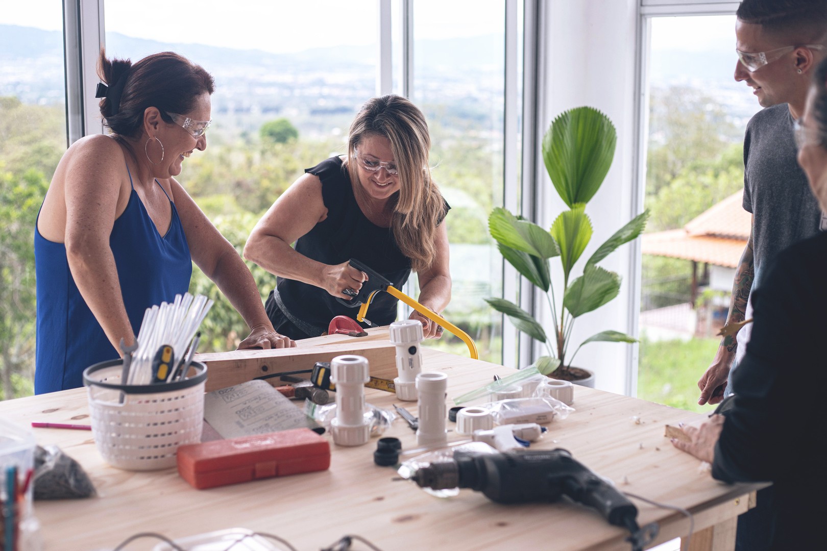 two women smile and laugh while sawing a piece of wood as colleagues admire their handiwork