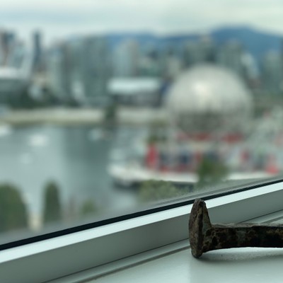 a rusted railroad spike sits on a ledge in front of a window overlooking Vancouver