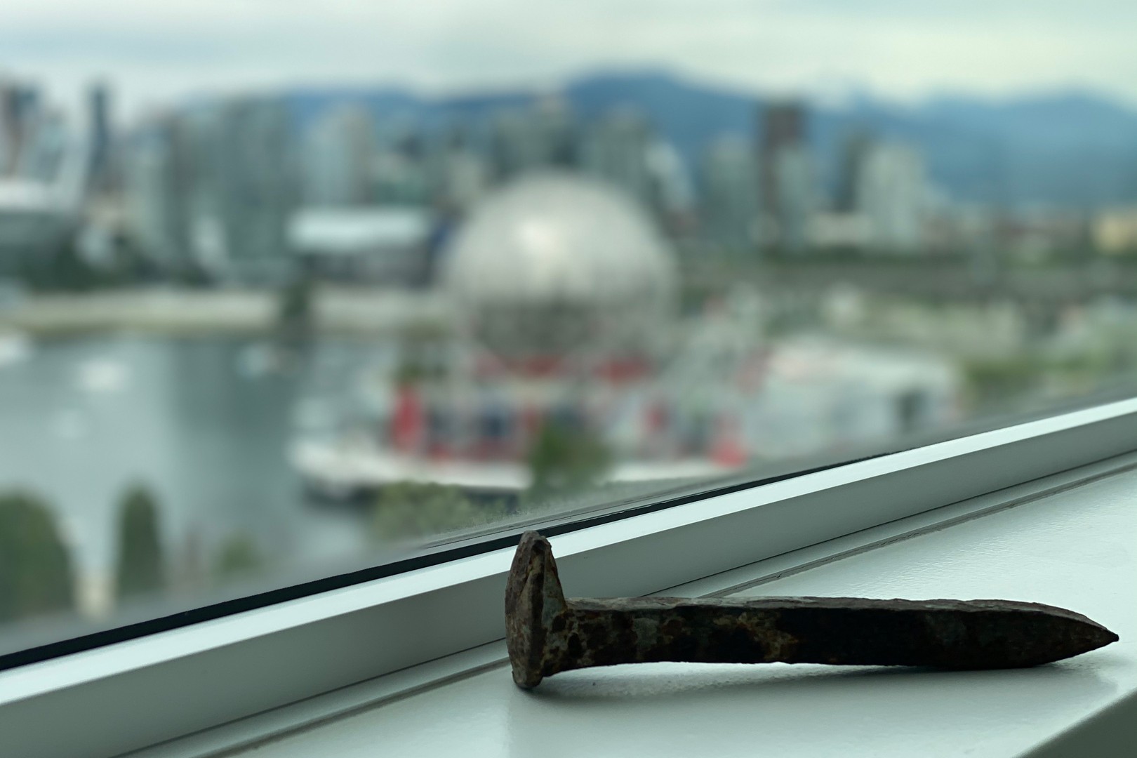 a rusted railroad spike sits on a ledge in front of a window overlooking Vancouver