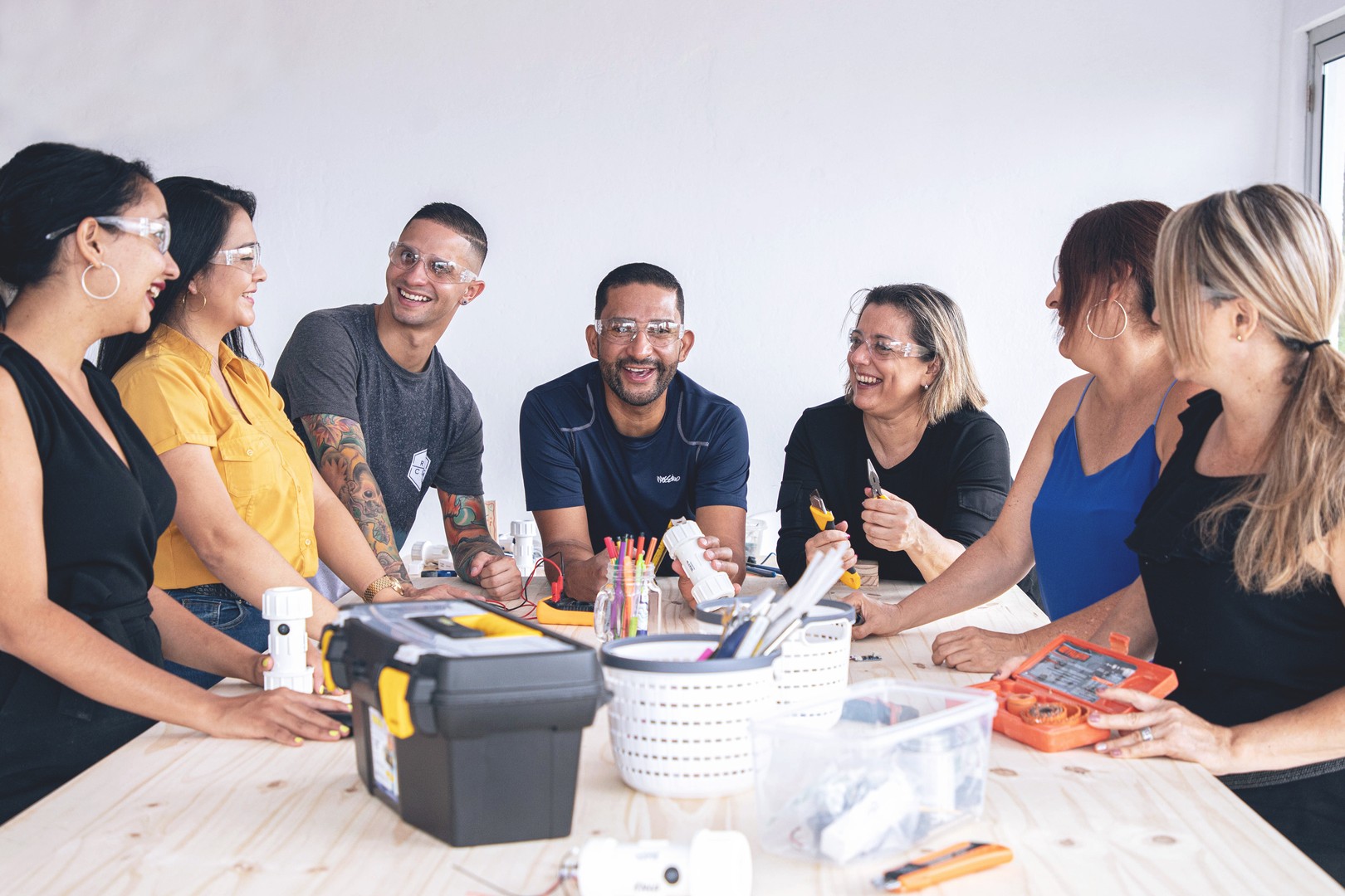 a diverse team of seven men and women standing around a wooden table smiling and laughing