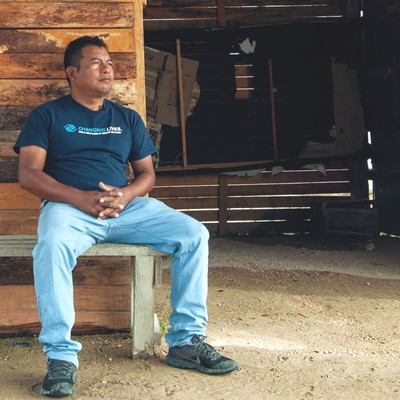 enoc, wearing jeans and a t-shirt, sits on a wooden bench in his garage