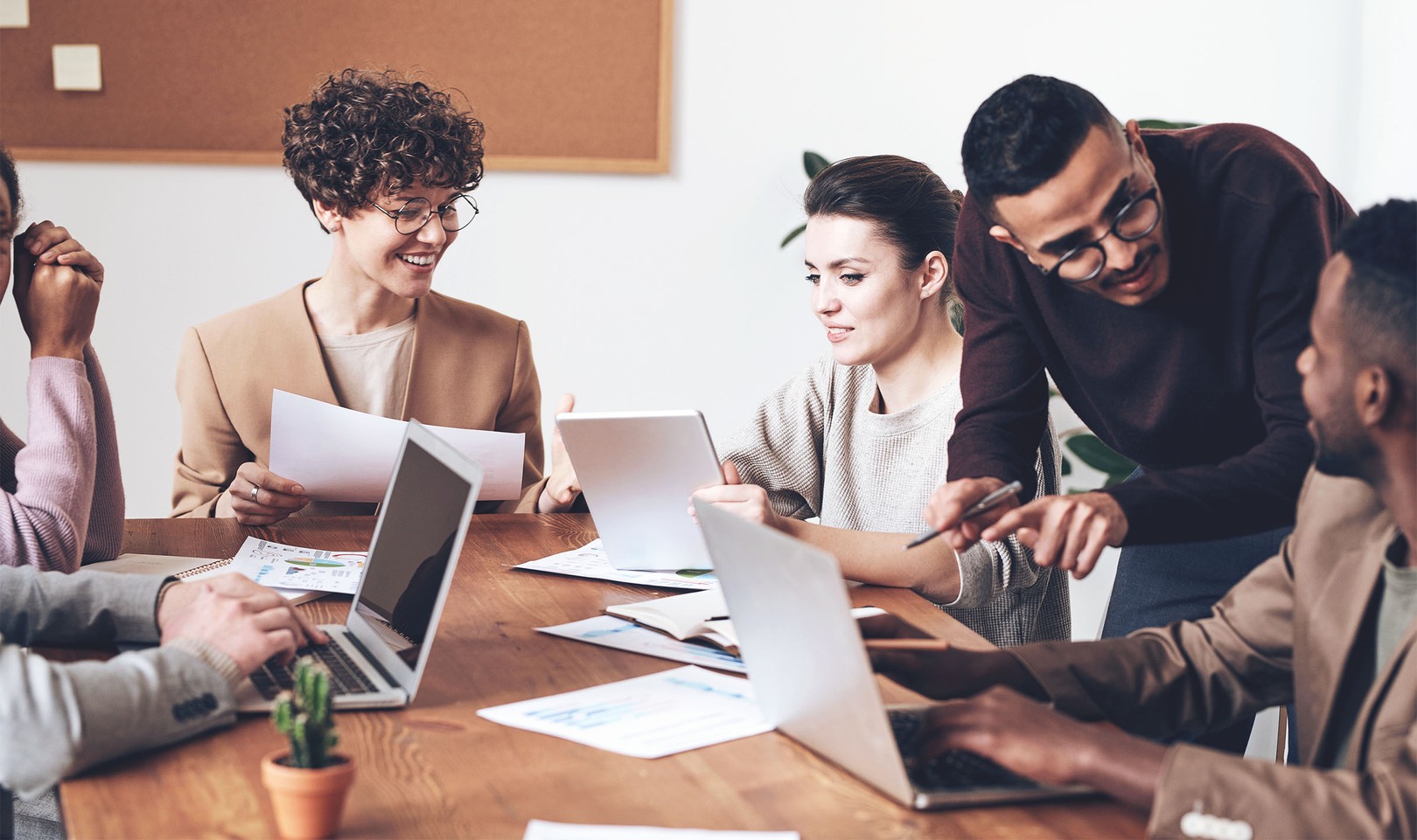 six people from a multigenerational and multicultural team smile while collaborating around a wooden table